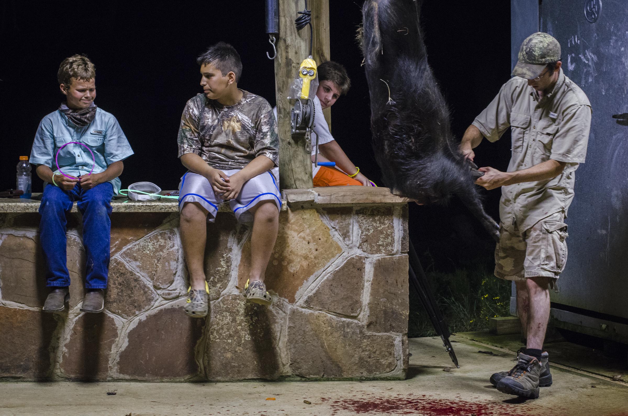 After bringing the dead pig back to camp, Garay skins it as Miguel and two fellow campers, from left, Cristian Salinas and Tristan Hardin, look on. The kids take home some of the meat they harvest; some of it is kept to feed future camps. Miguel said he planned to have the pig’s skull mounted as a trophy. 