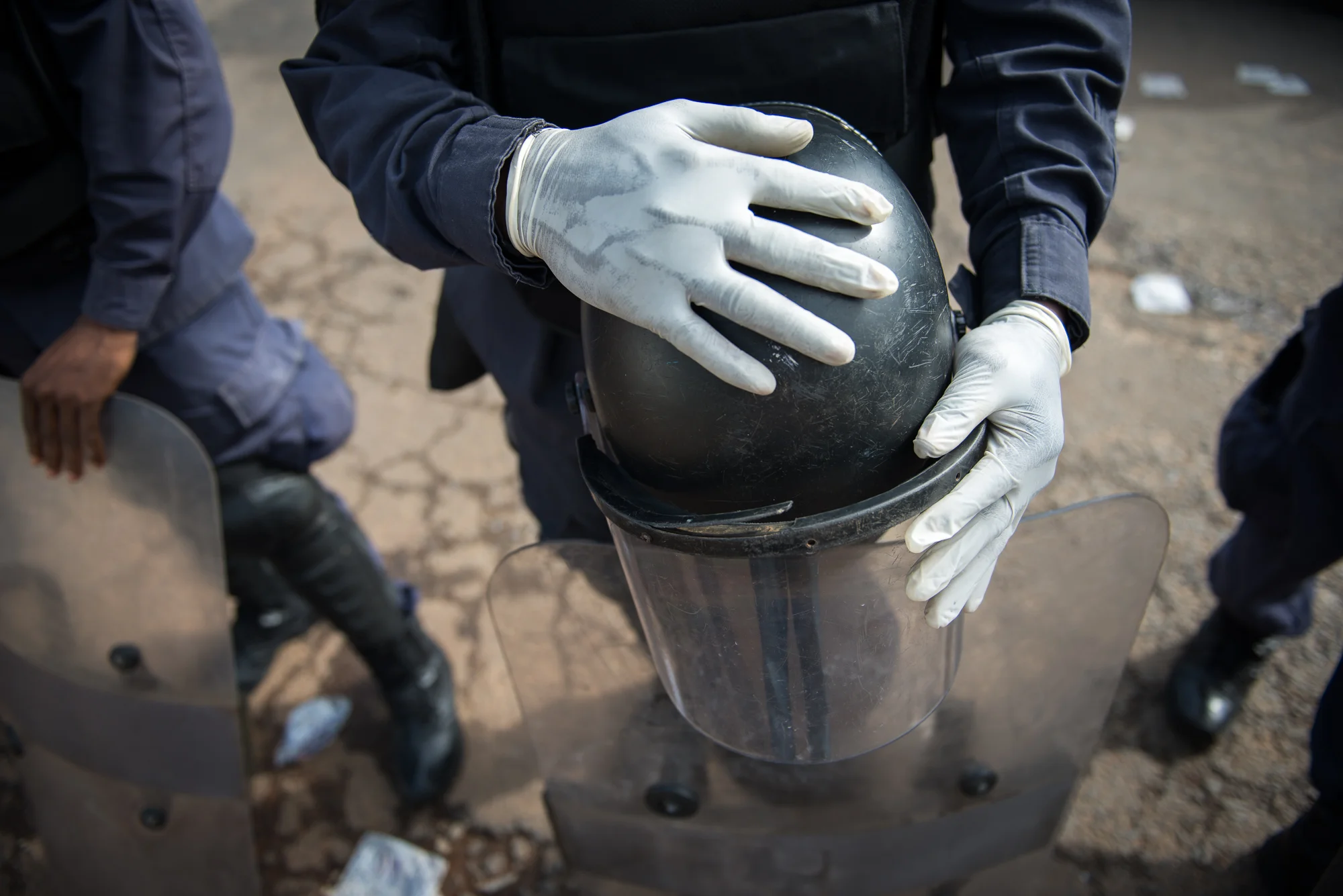 A Liberia National Police officer dressed in riot gear holds his helmet and shield following a large student demonstration in Monrovia. The officer, who refused to give his name, said he wore latex gloves in light of the recent return of Ebola cases in the country.
