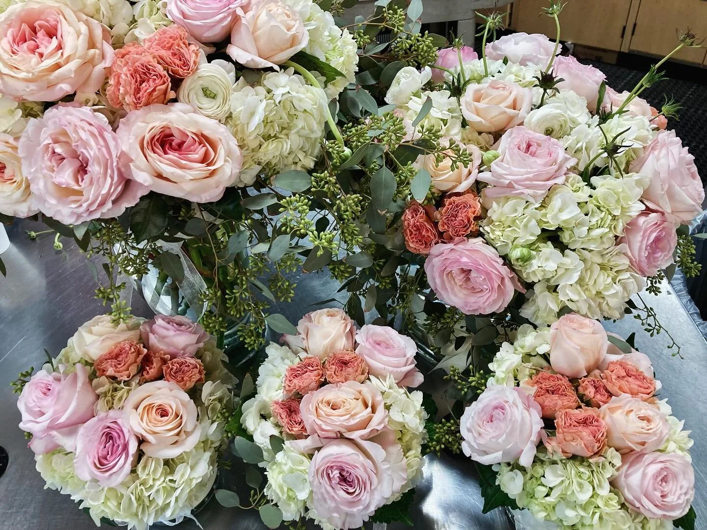 English Garden Roses, Hydrangea, Ranunculus and Seeded Eucalyptus in ribbon trimmed vases.