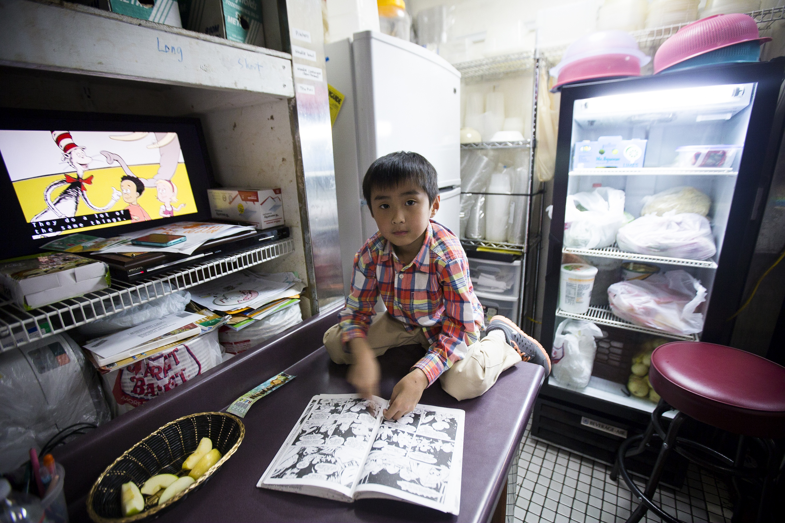  Henry Kyaw, 7. The son of Sai Kyaw reading comic books in a corner of the kitchen at Yoma. By Ann Wang 