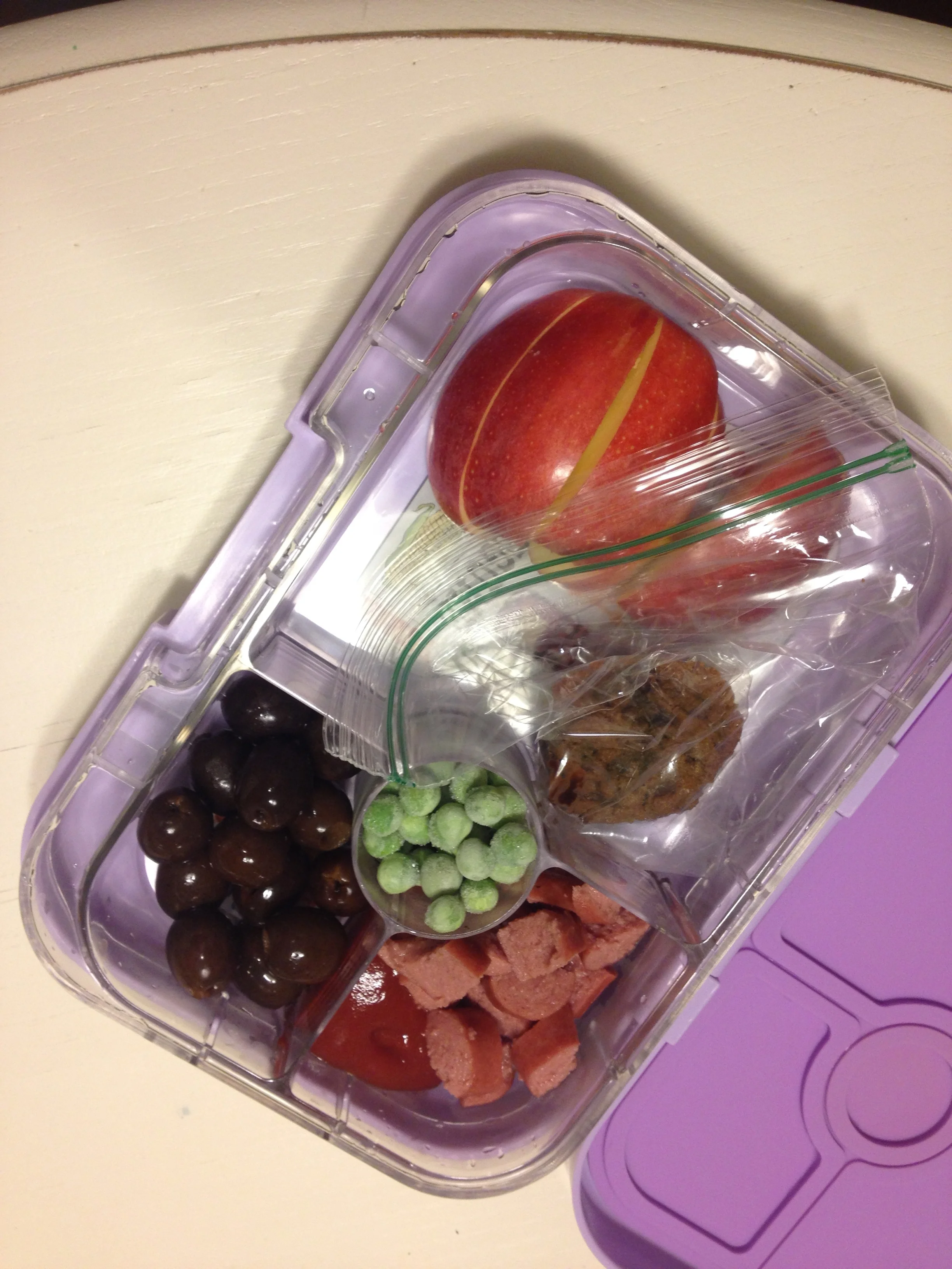 Grass-fed beef hotdog, black olives, cut apple, frozen peas, and a sunflower seed/chocolate chip cookie
