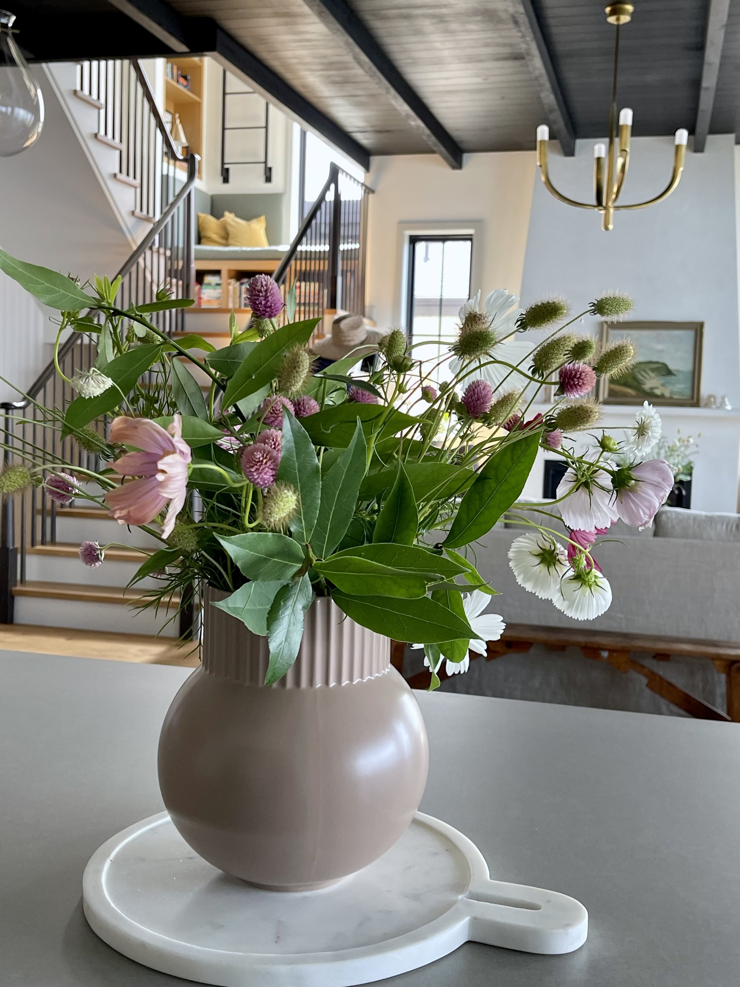 Pink vase of flowers on kitchen island with staircase in background