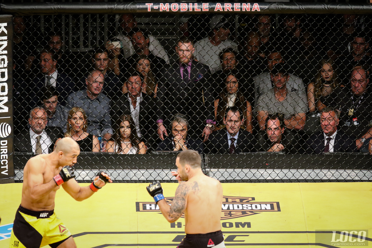 Conor McGregor remains standing and watches intently as Jose Aldo and Frankie Edgar square off at UFC 200.