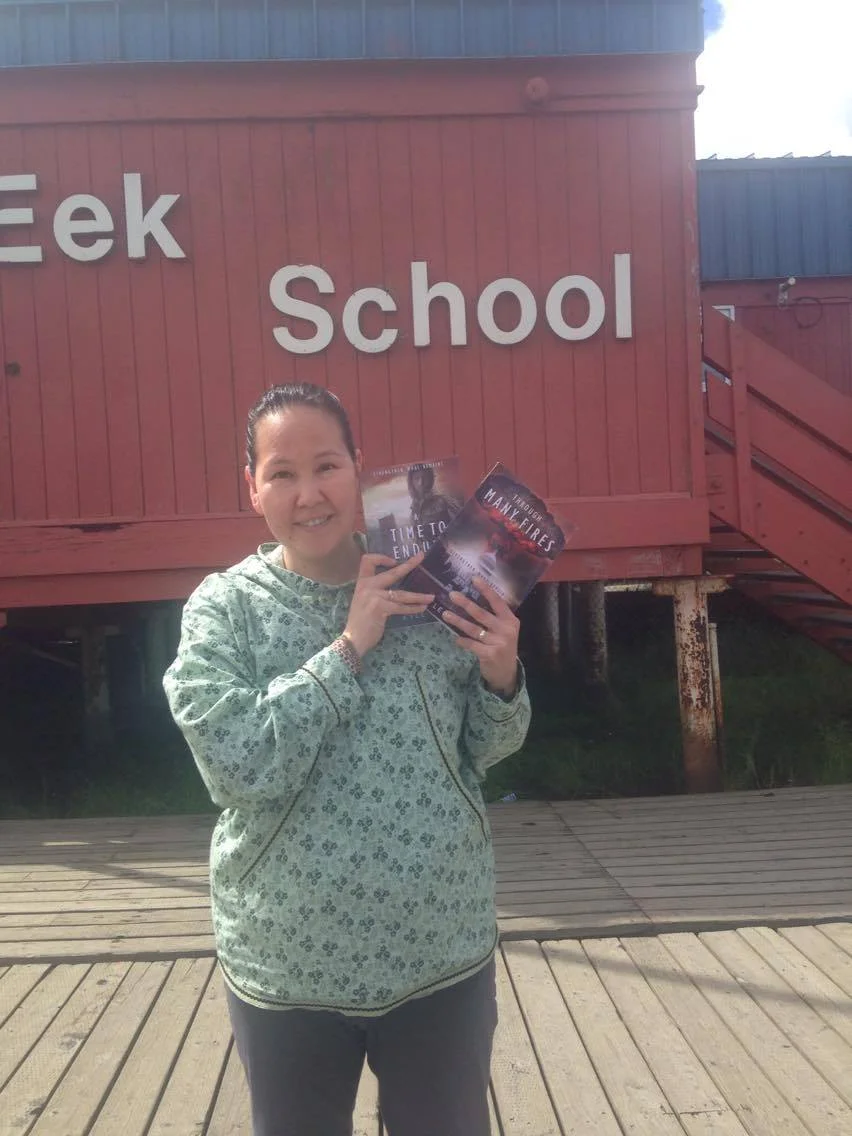Loni from Eek, Alaska, in front of the village school with Through Many Fires and A Time to Endure .