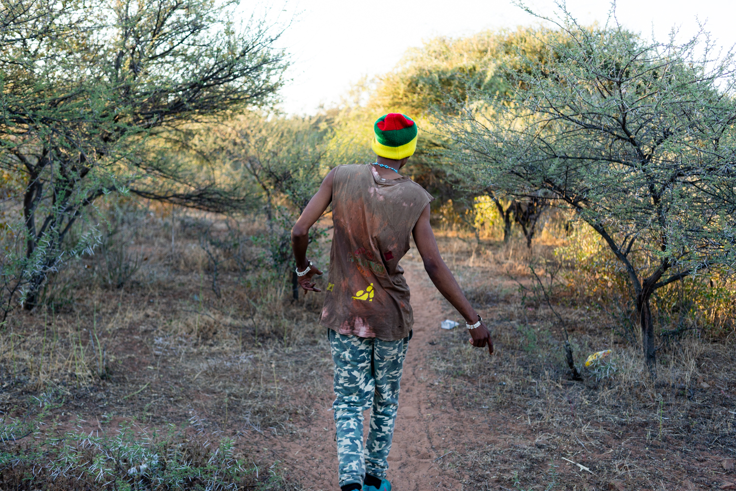 Alphynho walks along a dirt path back to his house. He always has music playing on his phone in his pocket and sings a dances wherever he goes.