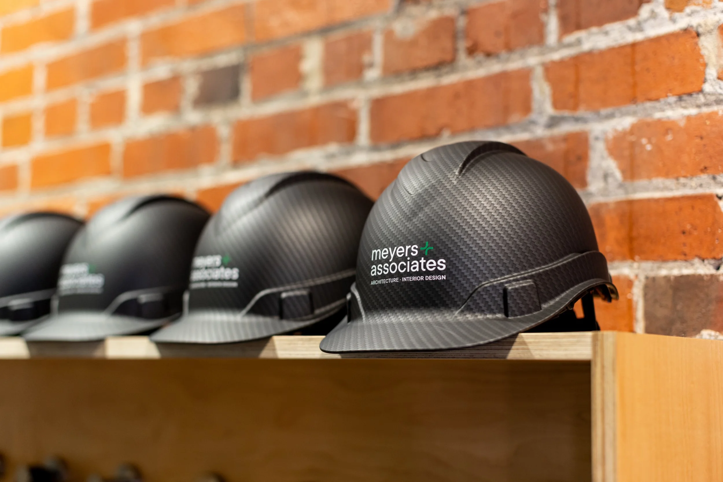 Black rubber slides with the logo 'meyers associates architecture interior design' on a wooden shelf against a brick wall.