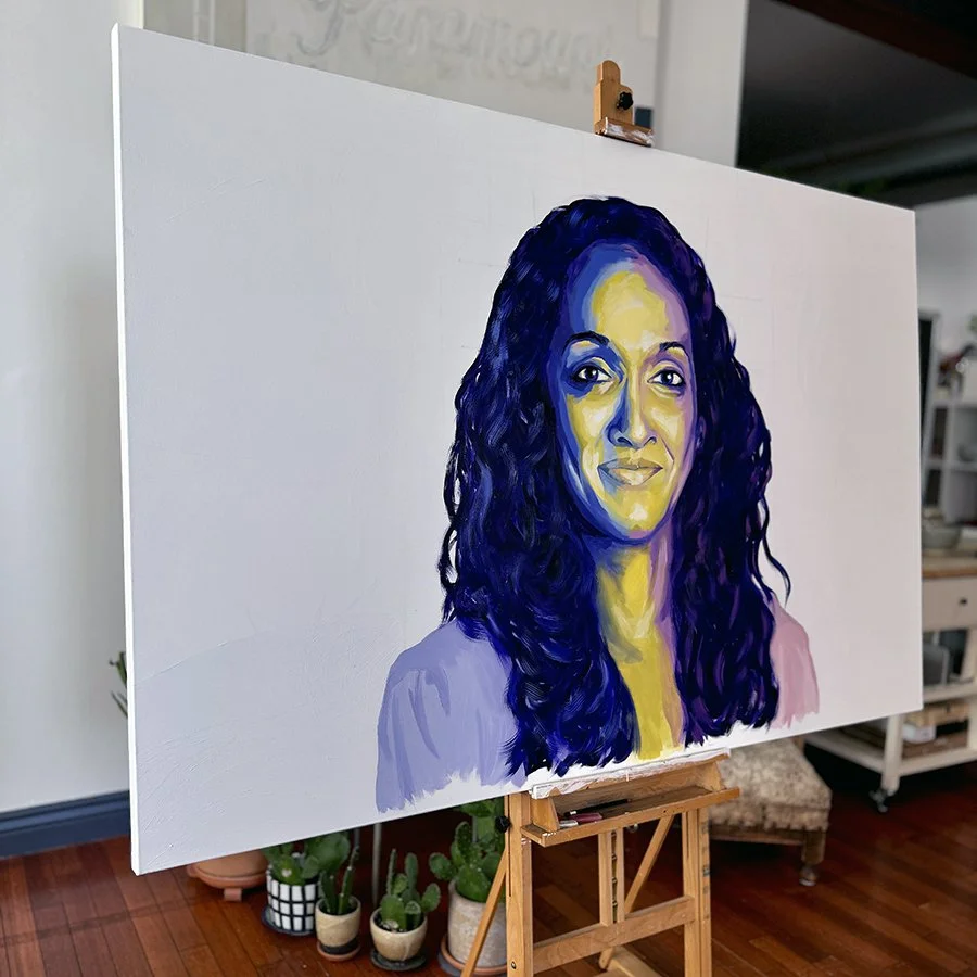 Portrait painting of a woman with dark curly hair, painted with bold shades of blue and yellow, on a large canvas in an art studio.