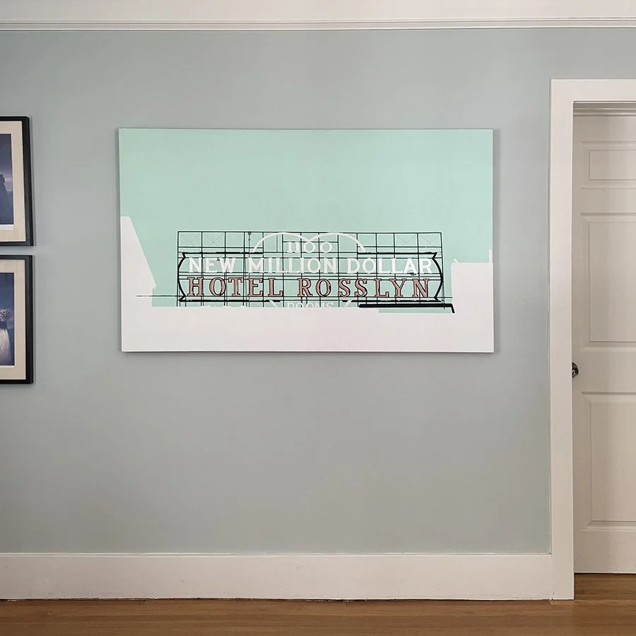 A wall with a large framed picture of a hotel sign reading "Hotel Rosslyn" with a background of sky and clouds.