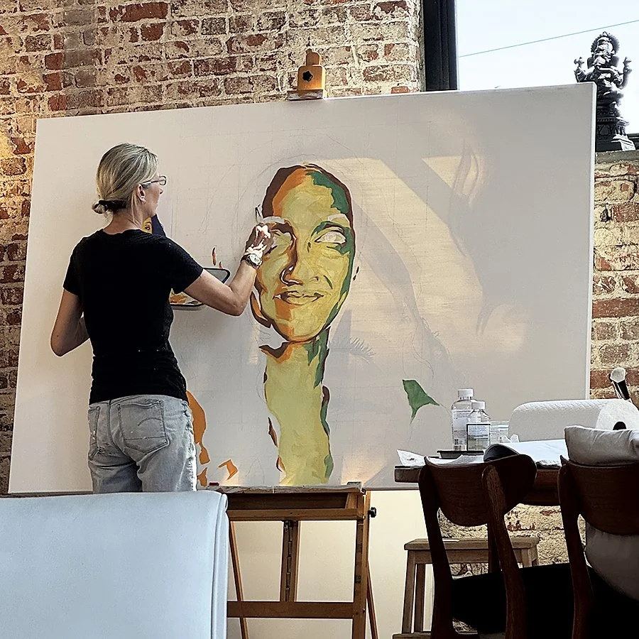 Artist working on a portrait of a woman with a smile, on a large white canvas in a studio with brick walls.