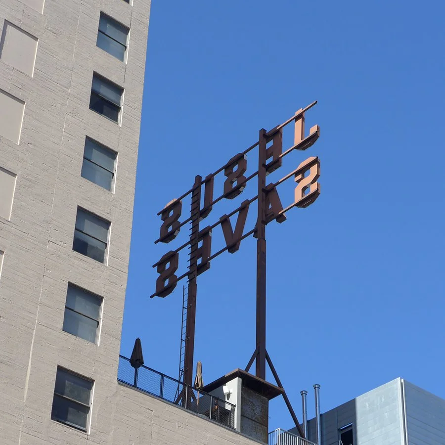 Old metal hotel sign reading 'Hotel Biltmore' mounted on a rooftop against a clear blue sky.