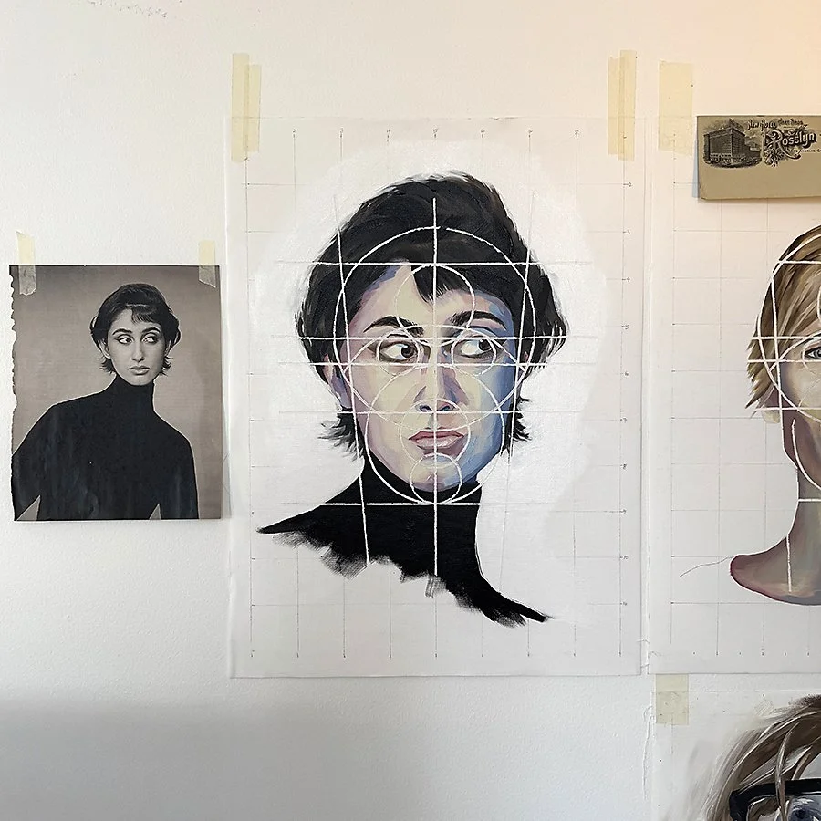 A grid sketch with a portrait of a woman with short dark hair and wearing a black turtleneck, featuring white circles and lines for artistic planning, with a reference black and white photo of the same woman taped to the wall on the left.