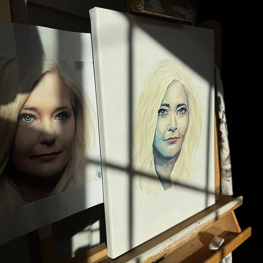 A side-by-side comparison of a photograph of a woman with blonde hair and blue eyes and an oil painting of the same woman, displayed on an easel with sunlight casting shadows on both.