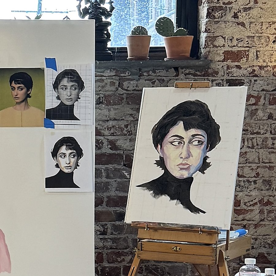 An art studio with a portrait of a woman on a canvas, showing a painted interpretation of a reference photo pinned on a white board. Two potted cacti sit on the window sill, and a brick wall is visible in the background.