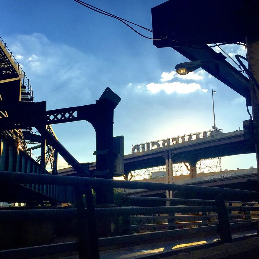 Silhouette of urban building and bridge structures against a blue sky with clouds.