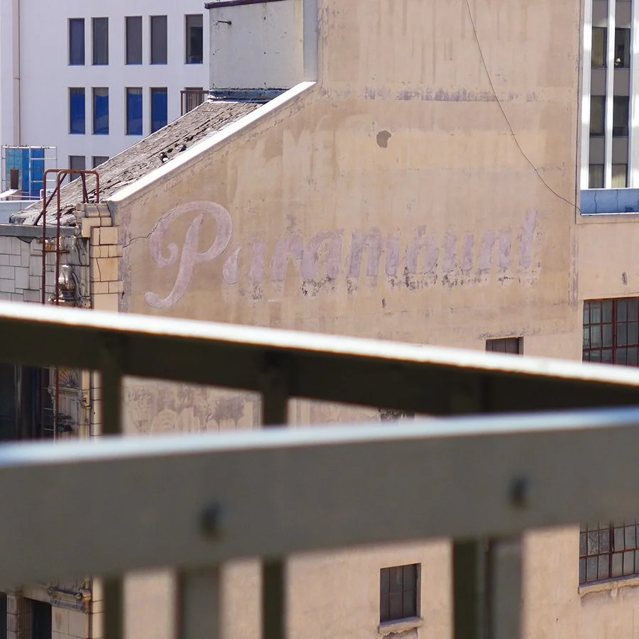 A faded pink sign on a beige building wall with the word 'Paramount' written in cursive.