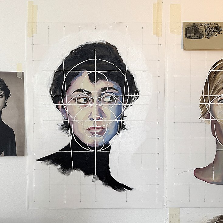 A grid sketch with a portrait of a woman with short dark hair and wearing a black turtleneck, featuring white circles and lines for artistic planning, with a reference black and white photo of the same woman taped to the wall on the left.