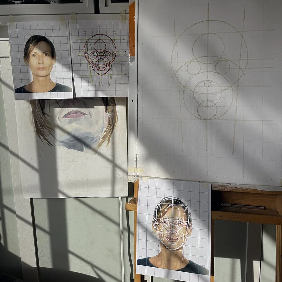 Photographs and sketches of a woman's face showing different facial drawing stages, with grid backgrounds for proportion guides, on a wall with sunlight casting shadows.