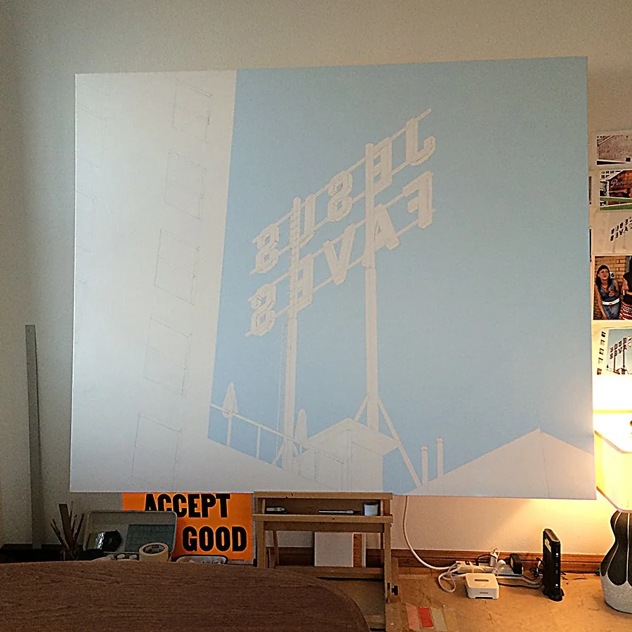 Projection of the Hollywood sign on a blank wall in a room, with a sign that says 'Accept Good' on the desk below.