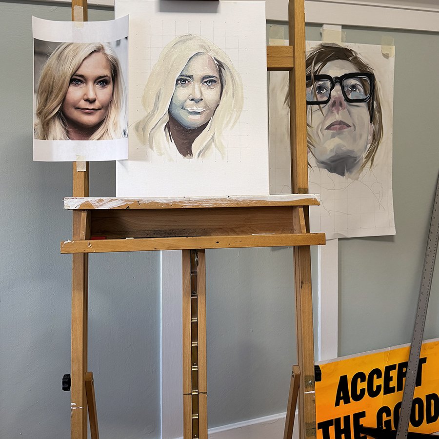 Three artistic portraits, including a completed photo-realistic painting of a woman with blonde hair, a partially finished sketch of a woman with blonde hair, and a caricature of a woman with glasses. The portraits are on an easel in an art studio.