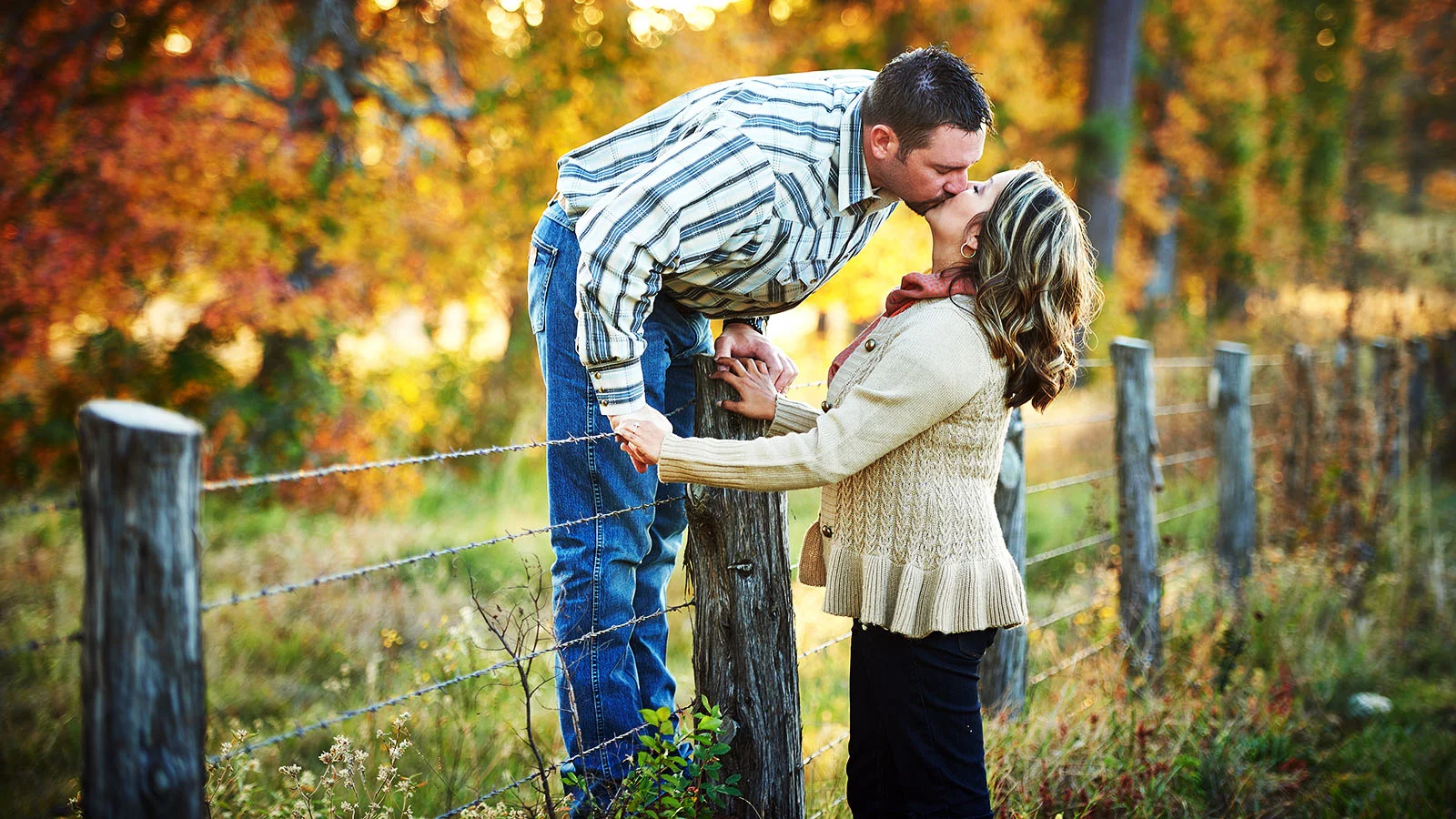 Engagement photo with groom on a fence kissing bride