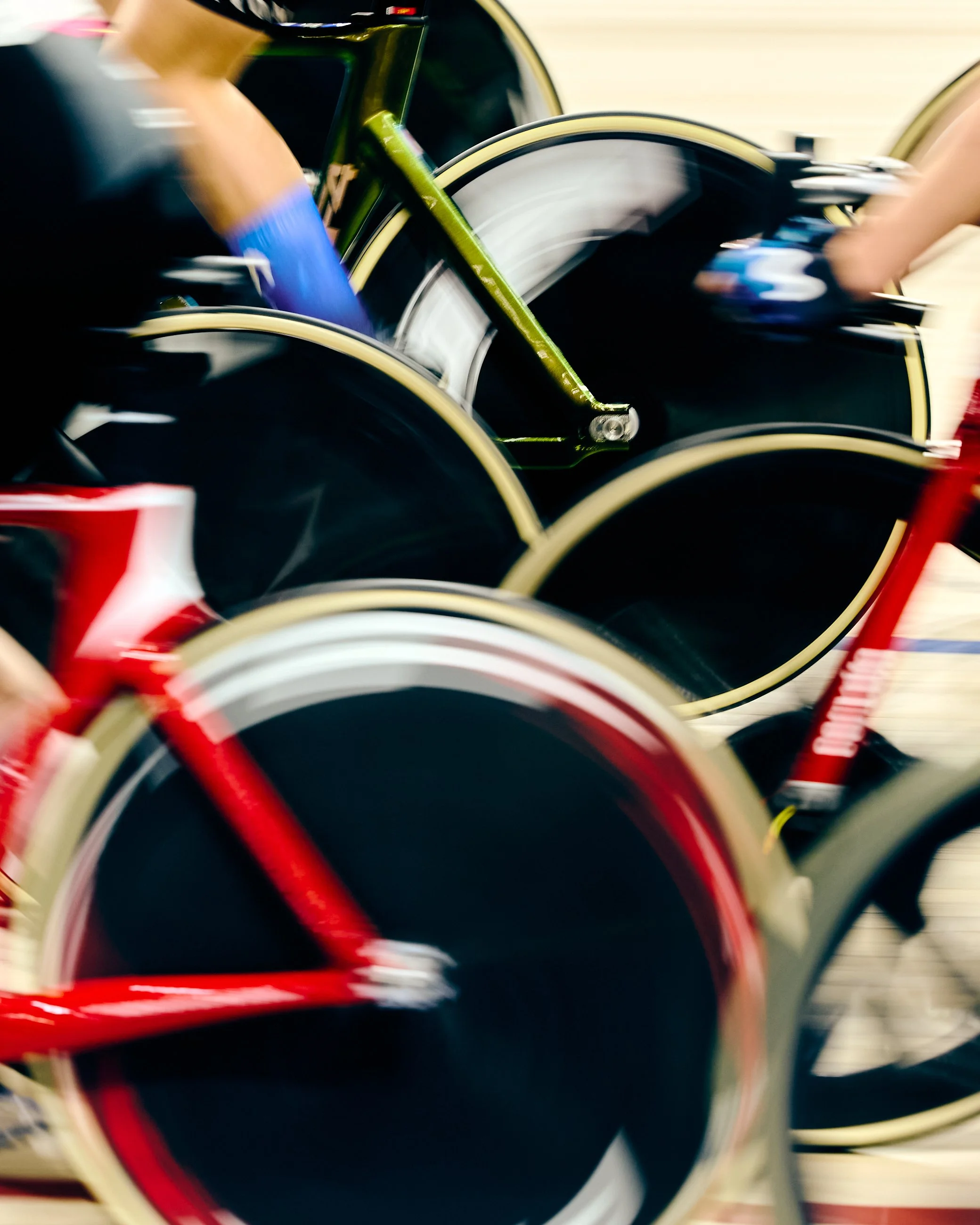 Close-up of several racing bicycles with blurred motion, emphasizing the wheels and frames, in red, green, and black colors.