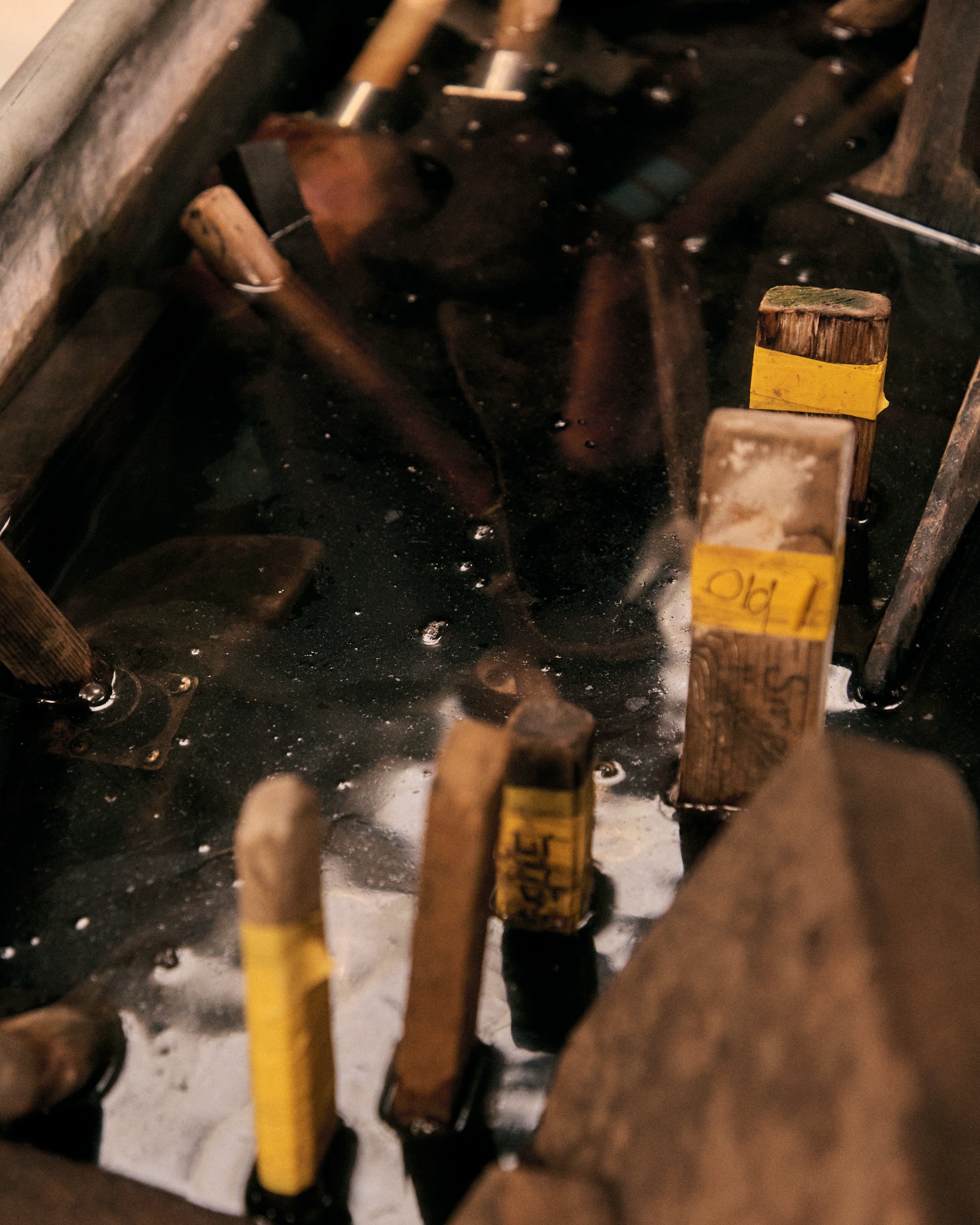 A close-up view of wooden stakes with yellow labels immersed in a dark liquid, possibly used in a fermentation or preservation process.