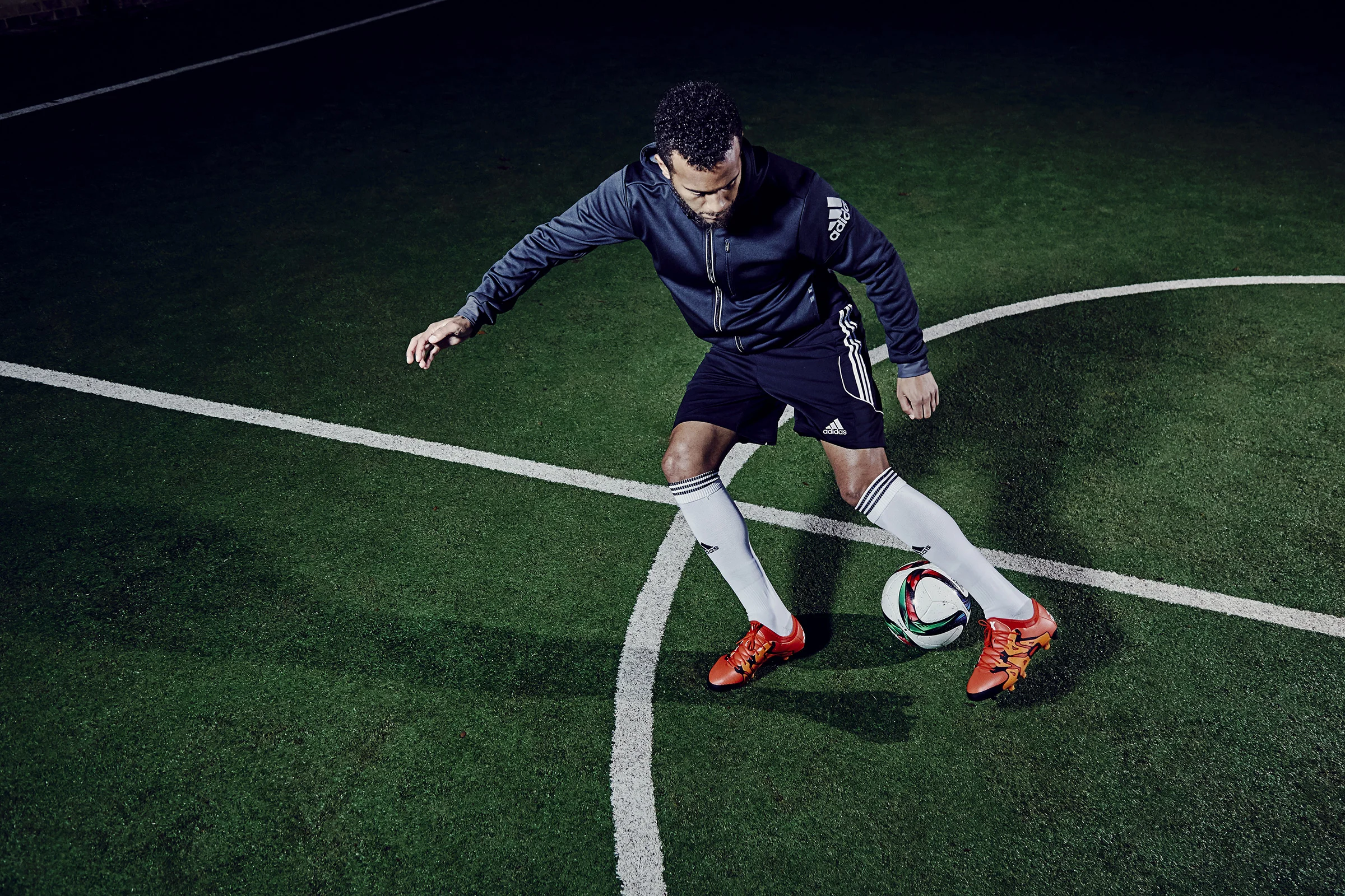 A man in sportswear practicing soccer on a dark green artificial turf field, balancing a soccer ball with his foot.