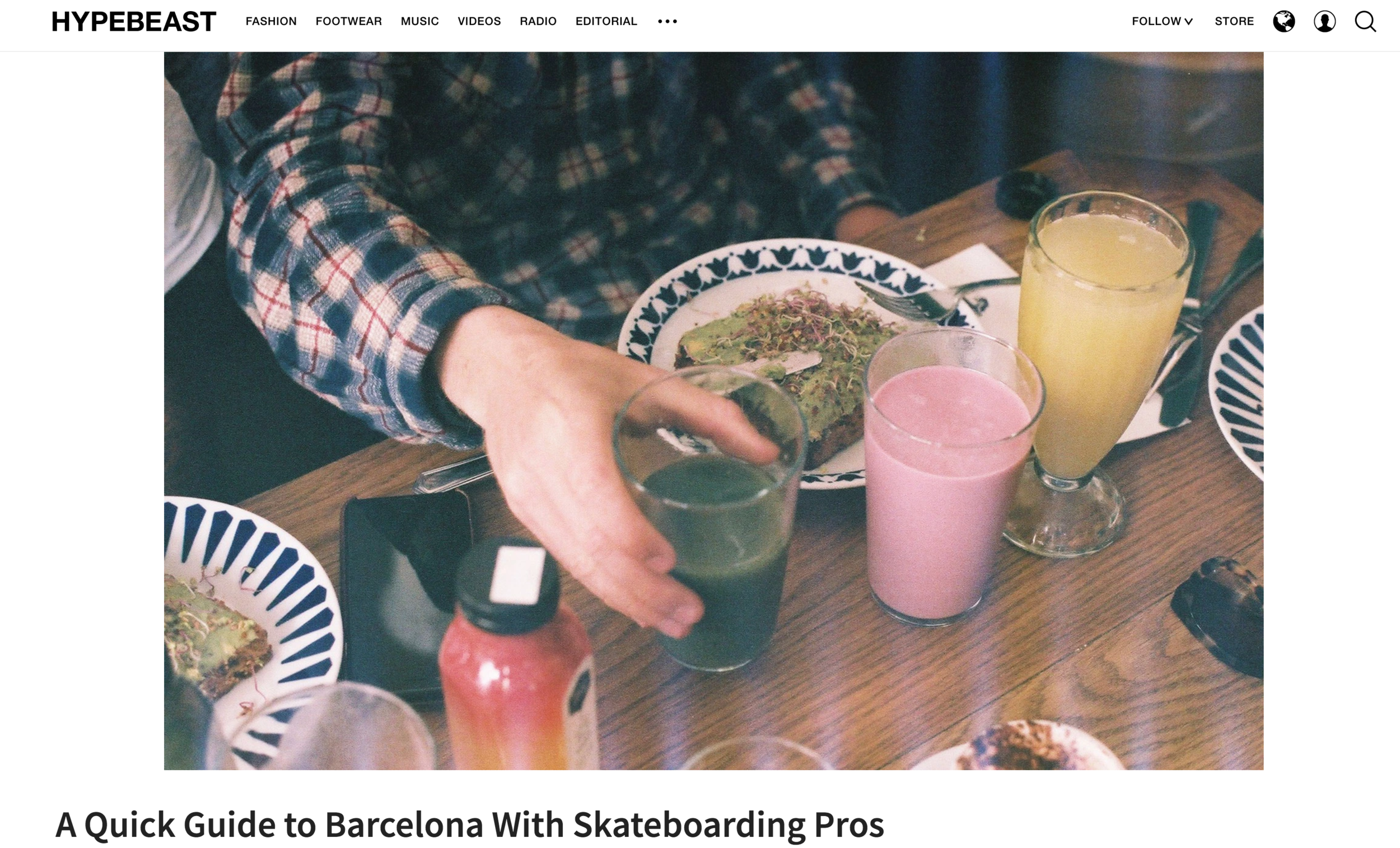 Person reaching for a glass of green beverage at a table with colorful drinks, plates of food, and a phone.