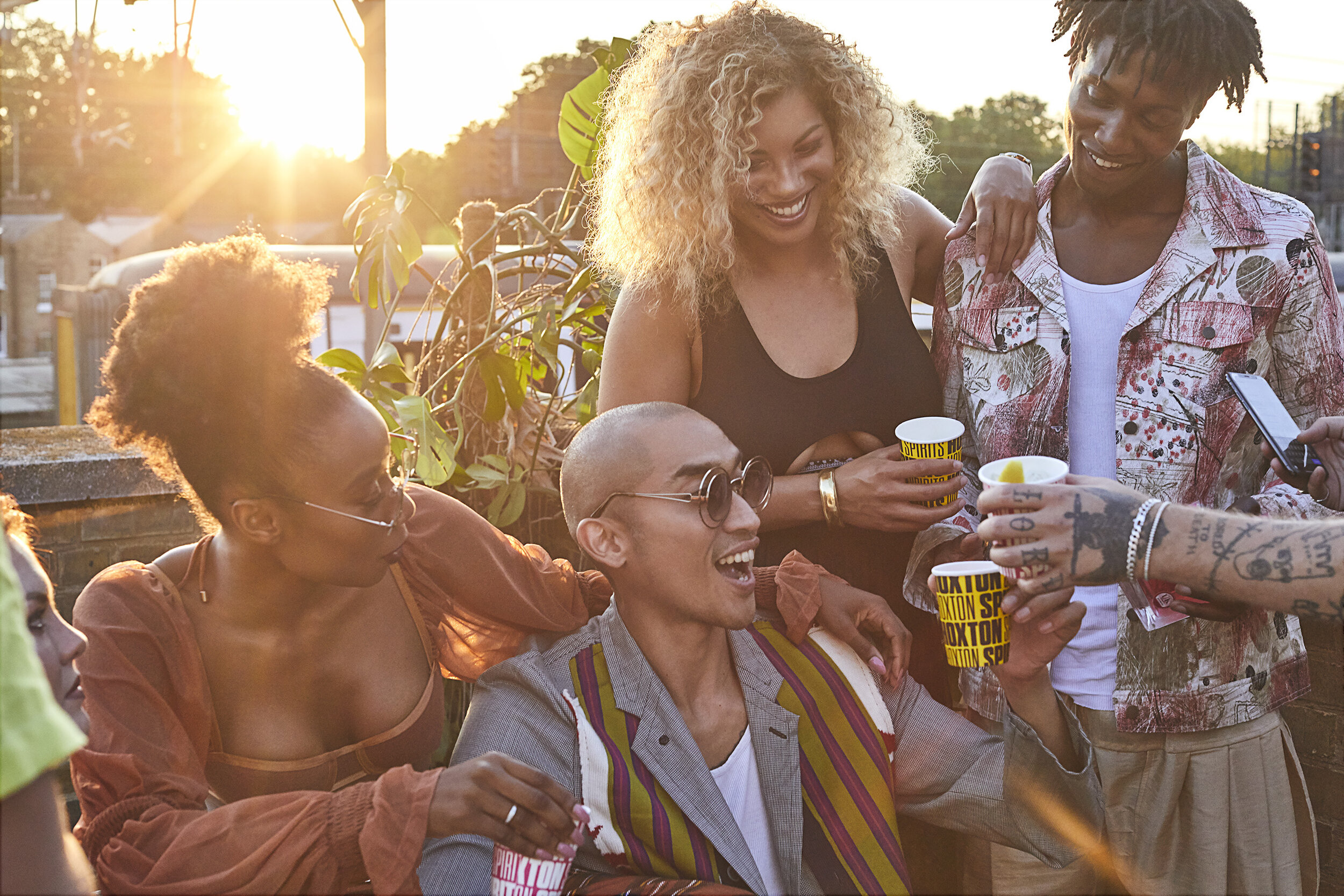 Group of friends enjoying drinks and socializing outdoors during sunset, smiling and having a good time.