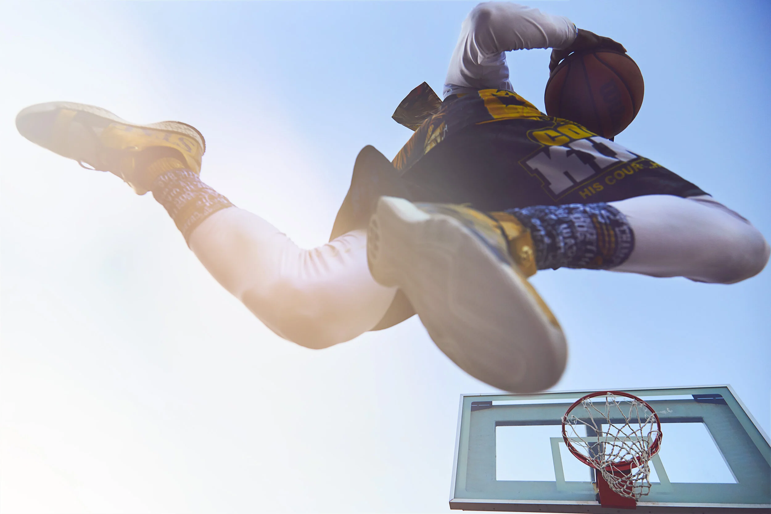Low-angle view of a basketball player dunking into a hoop on an outdoor court, with a clear blue sky background.