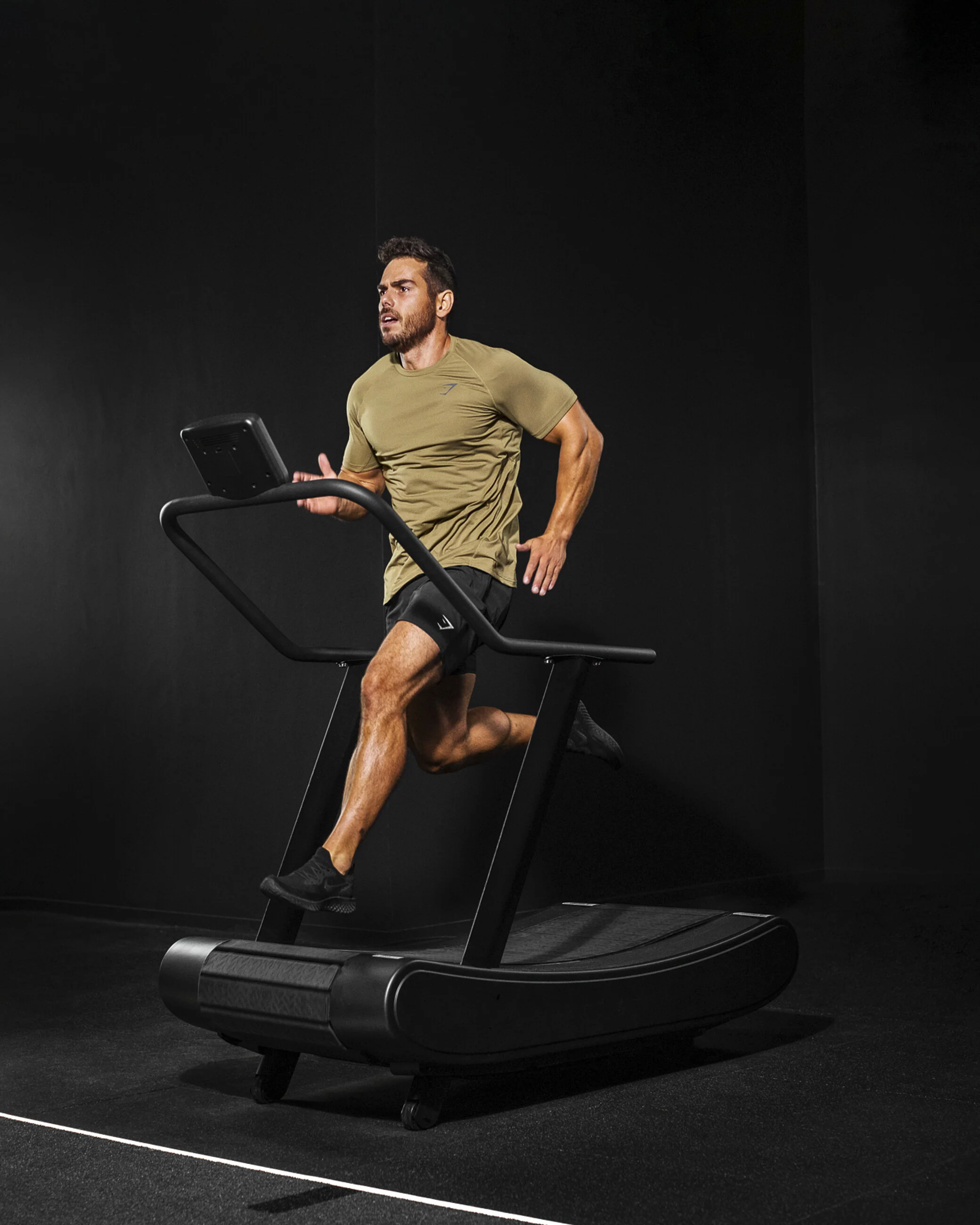 Man running on a treadmill in a fitness room with black walls.