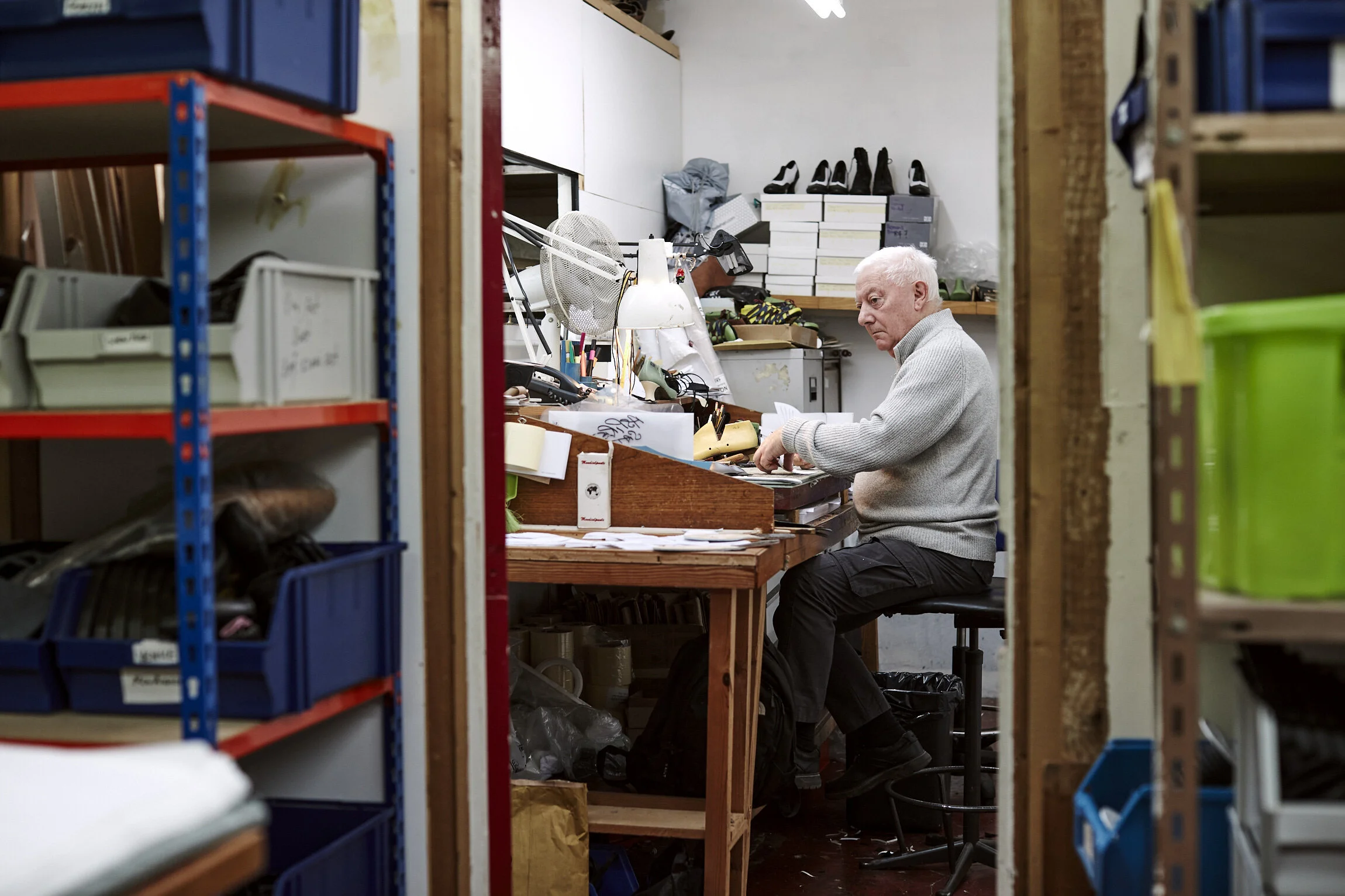 Older man working at a cluttered workspace inside a storage room with shelves and boxes.