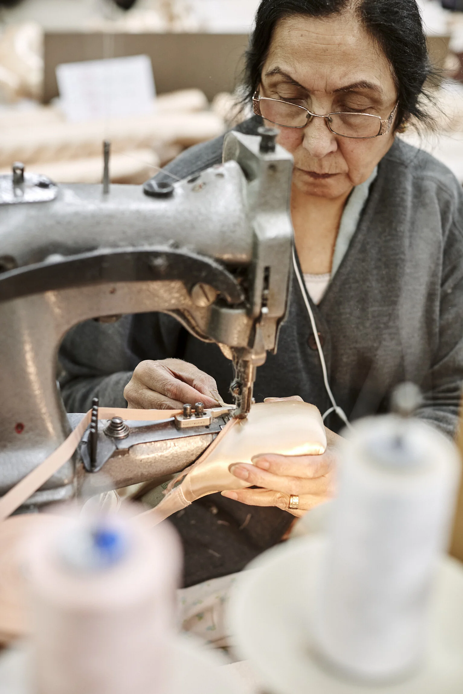 An elderly woman sewing or stitching a piece of fabric or material using a sewing machine in a workshop or textile studio.