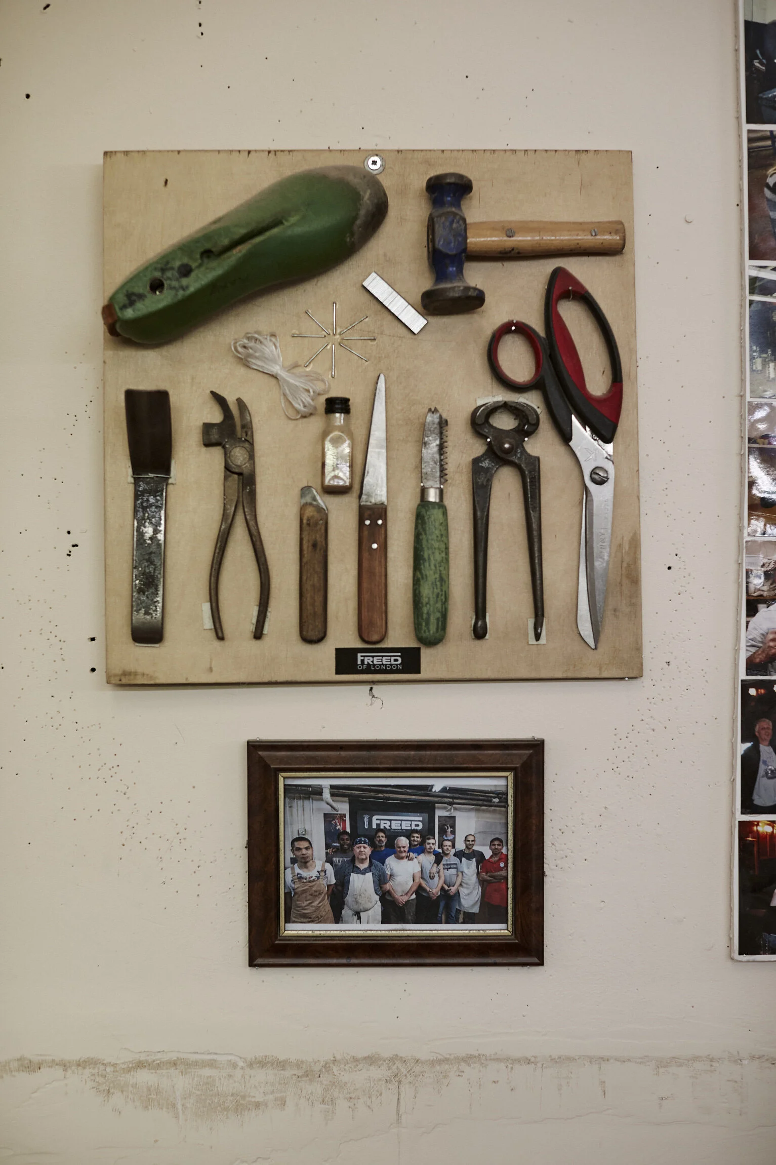 A wall display of various old tools mounted on a wooden board, including knives, scissors, pliers, a hammer, and a shoehorn, with a small framed photo of a group of people below it.