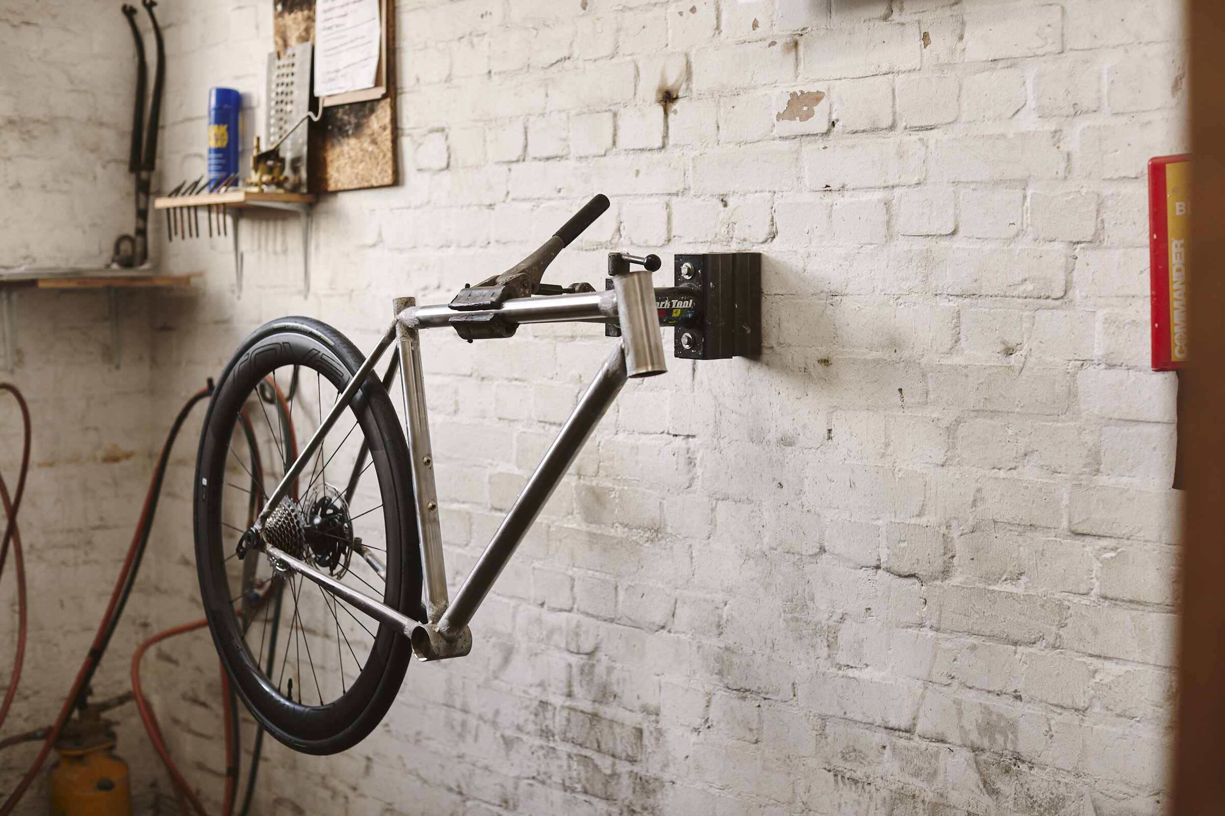 Bike frame mounted on a workshop wall, with tools and equipment in the background.