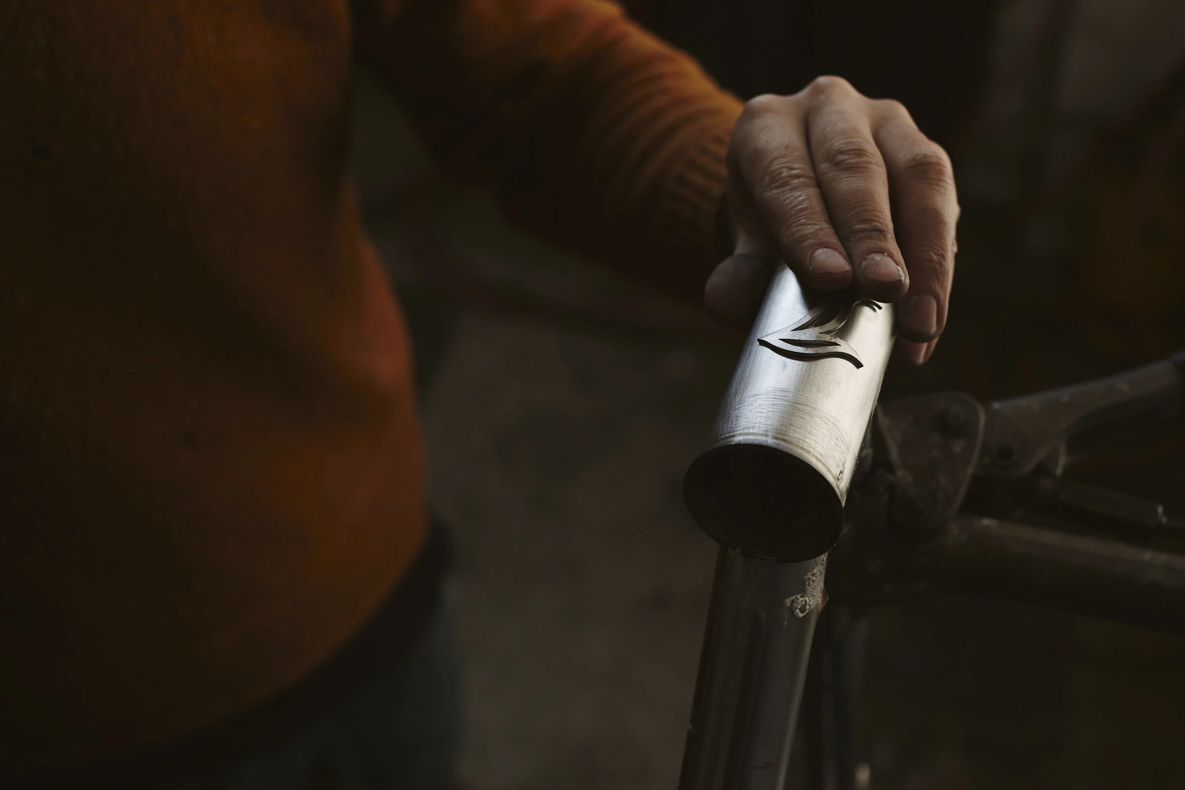 Close-up of a person's hand holding a metal tube with a design etched on it, near a bicycle handlebar.