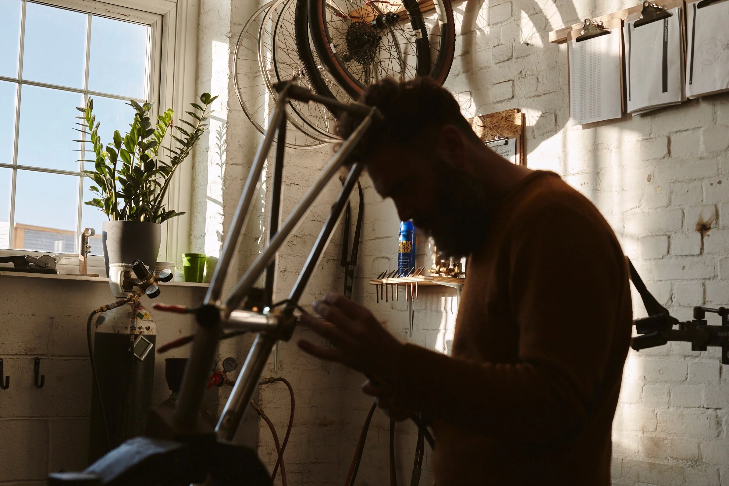 Person working on a bicycle in a workshop with sunlight coming through the window.