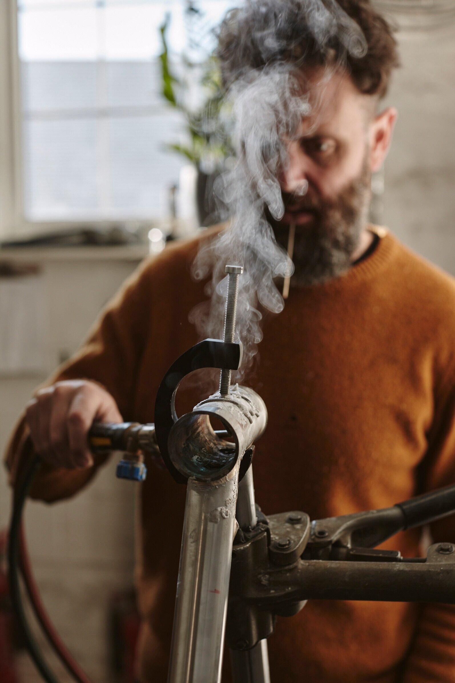 Man working on a motorcycle frame in a workshop, with smoke rising from the bike parts.