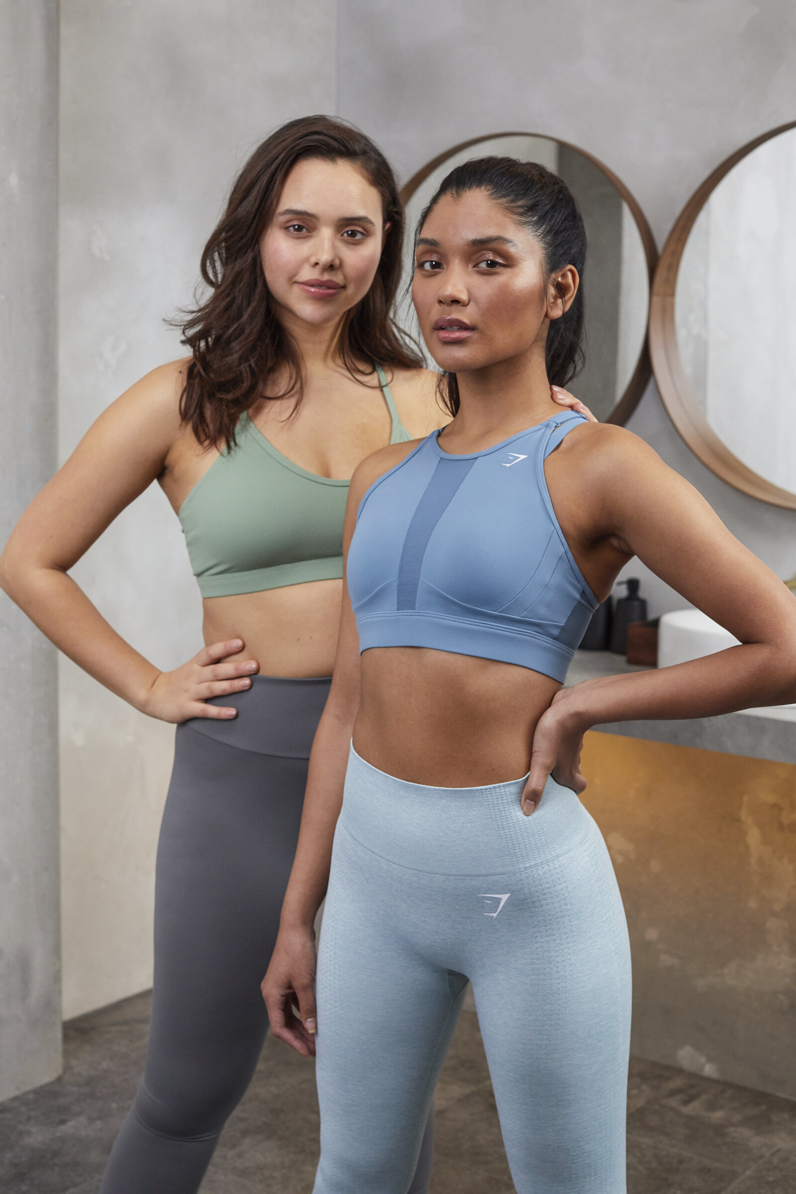 Two women in athletic wear posing indoors, with a mirror in the background.