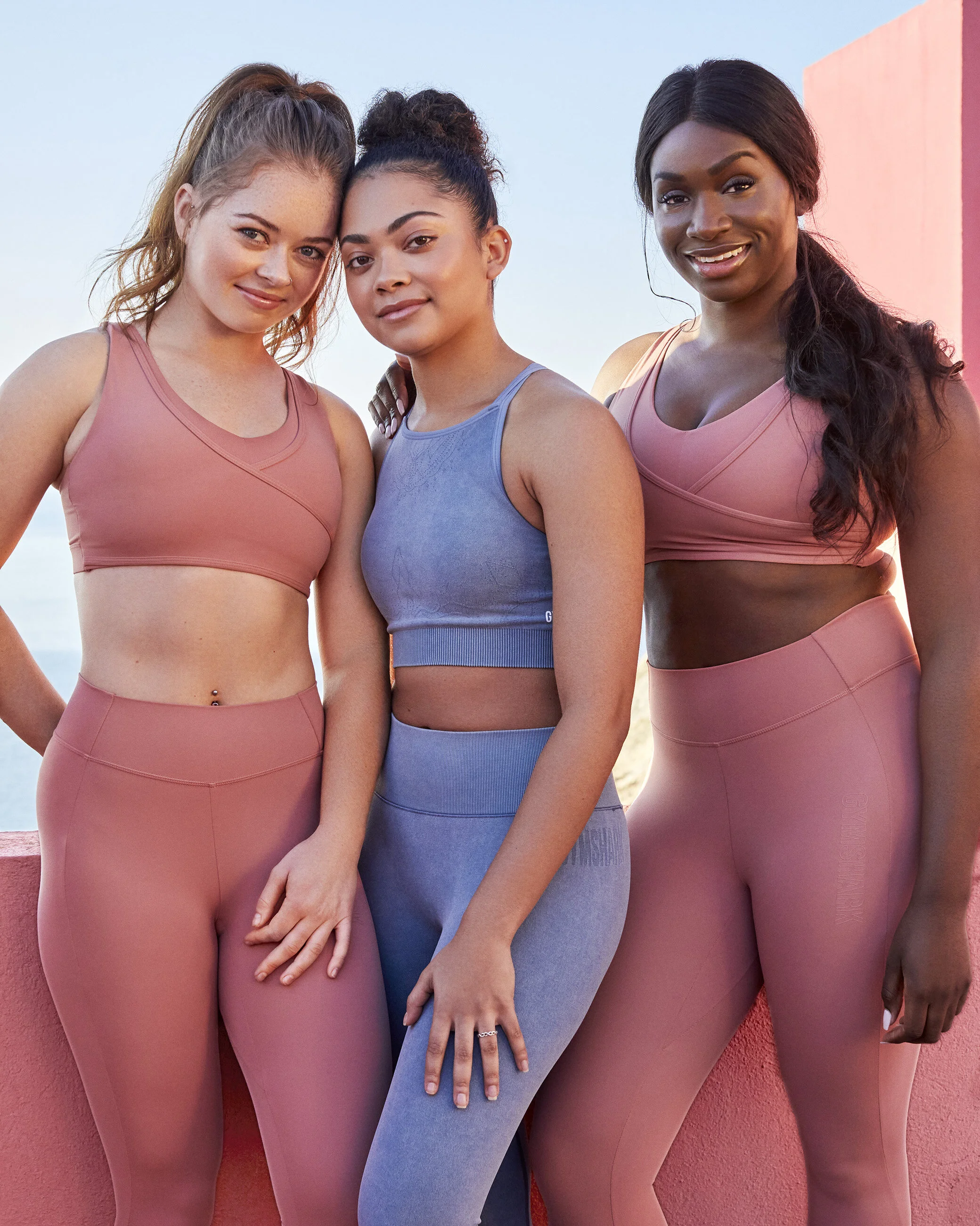 Three women in activewear standing together outdoors, smiling.