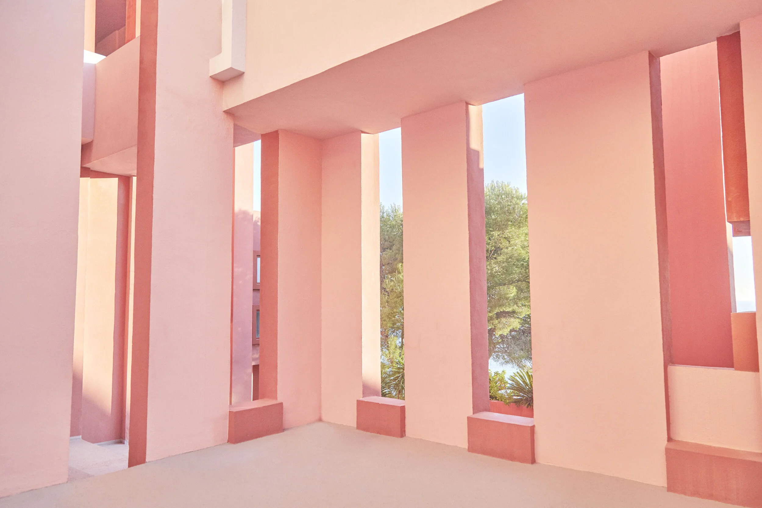 Interior view of a pink building with tall narrow windows and benches, with visible trees outside.