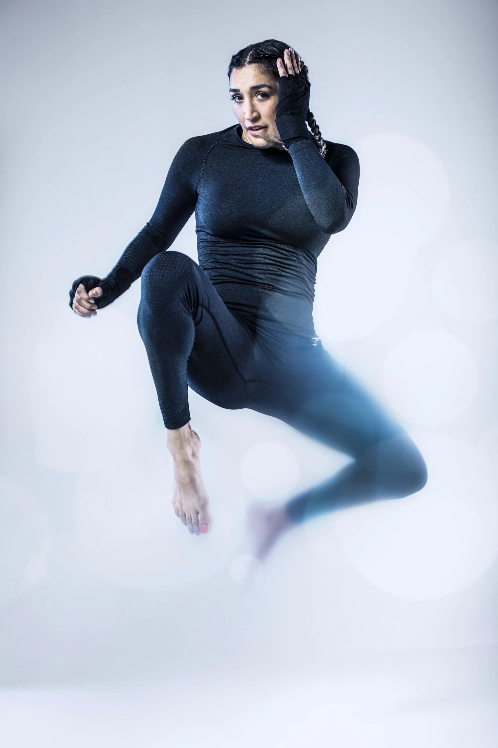 Woman in black athletic wear floating mid-air against neutral background, with a focused expression.