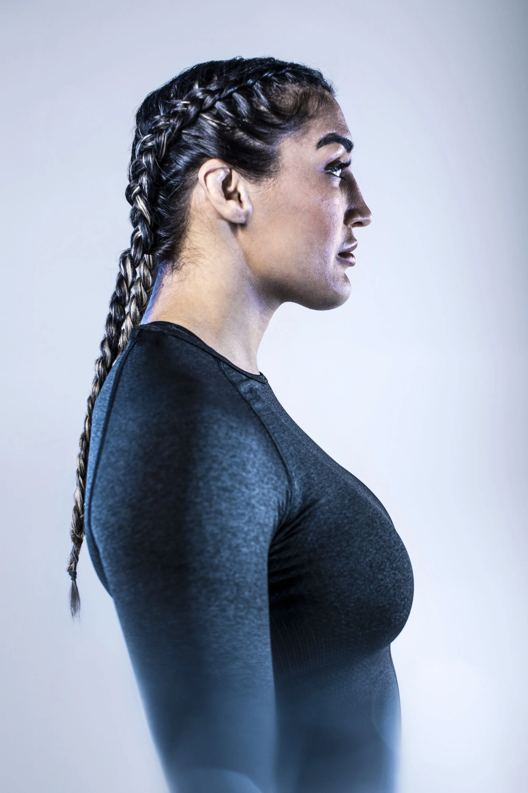 Profile of a woman with braided hair wearing a black athletic shirt, looking to the right against a plain light background.