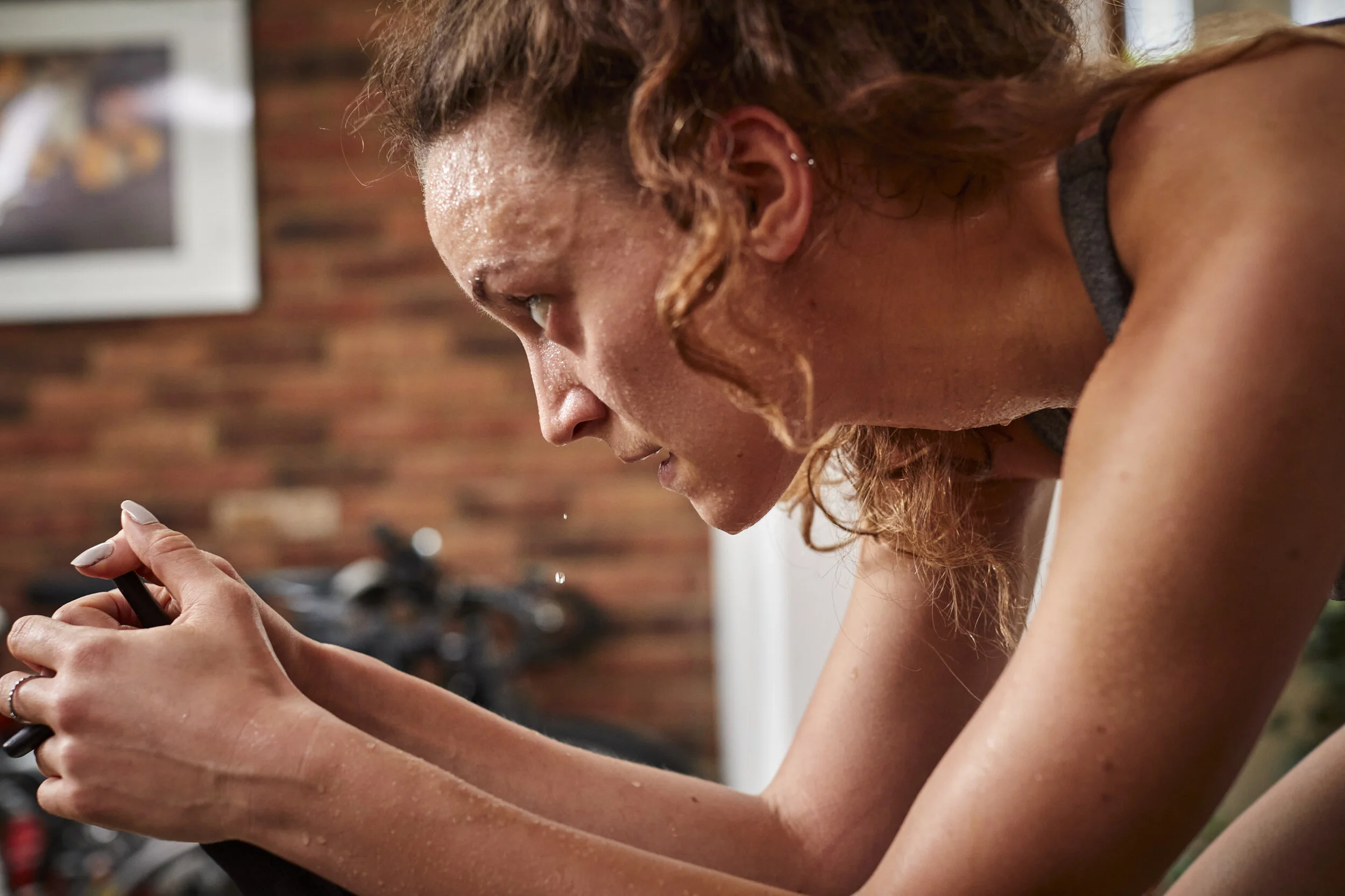 A woman with wet hair and sweat on her face, intensely focused while using a smartphone or fitness device during a workout.