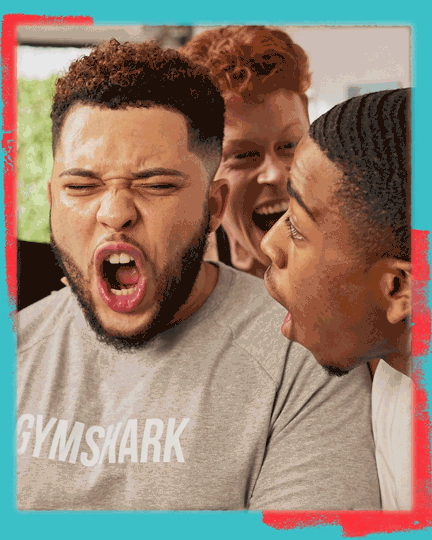 Three young men are making funny faces and appear to be playfully teasing each other, indoors with a window in the background.