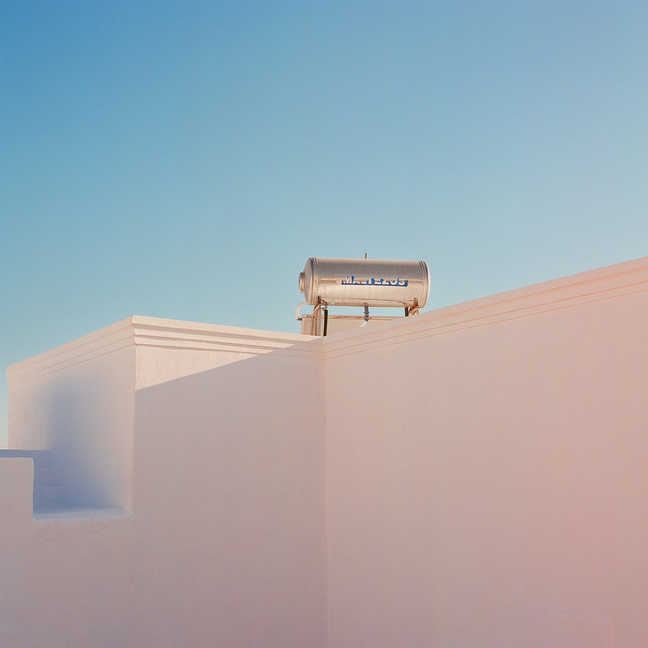 White building with curved edges against a clear blue sky, with a metallic water heater or tank mounted on the roof.