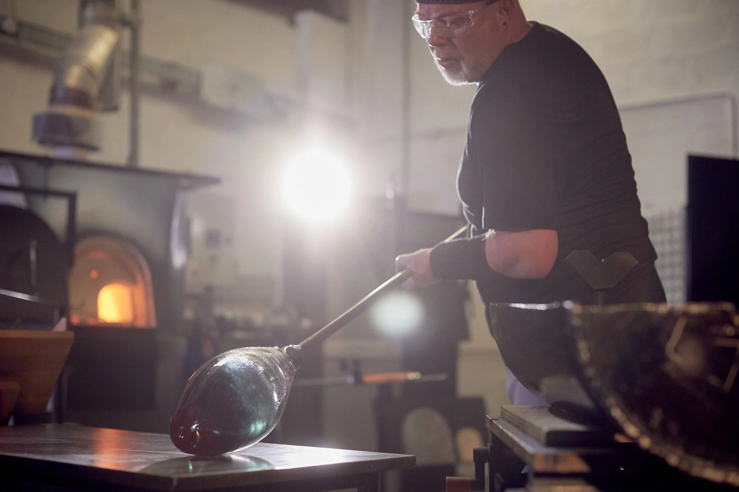 A blacksmith forging a glass bottle in a workshop, with a furnace glowing in the background.