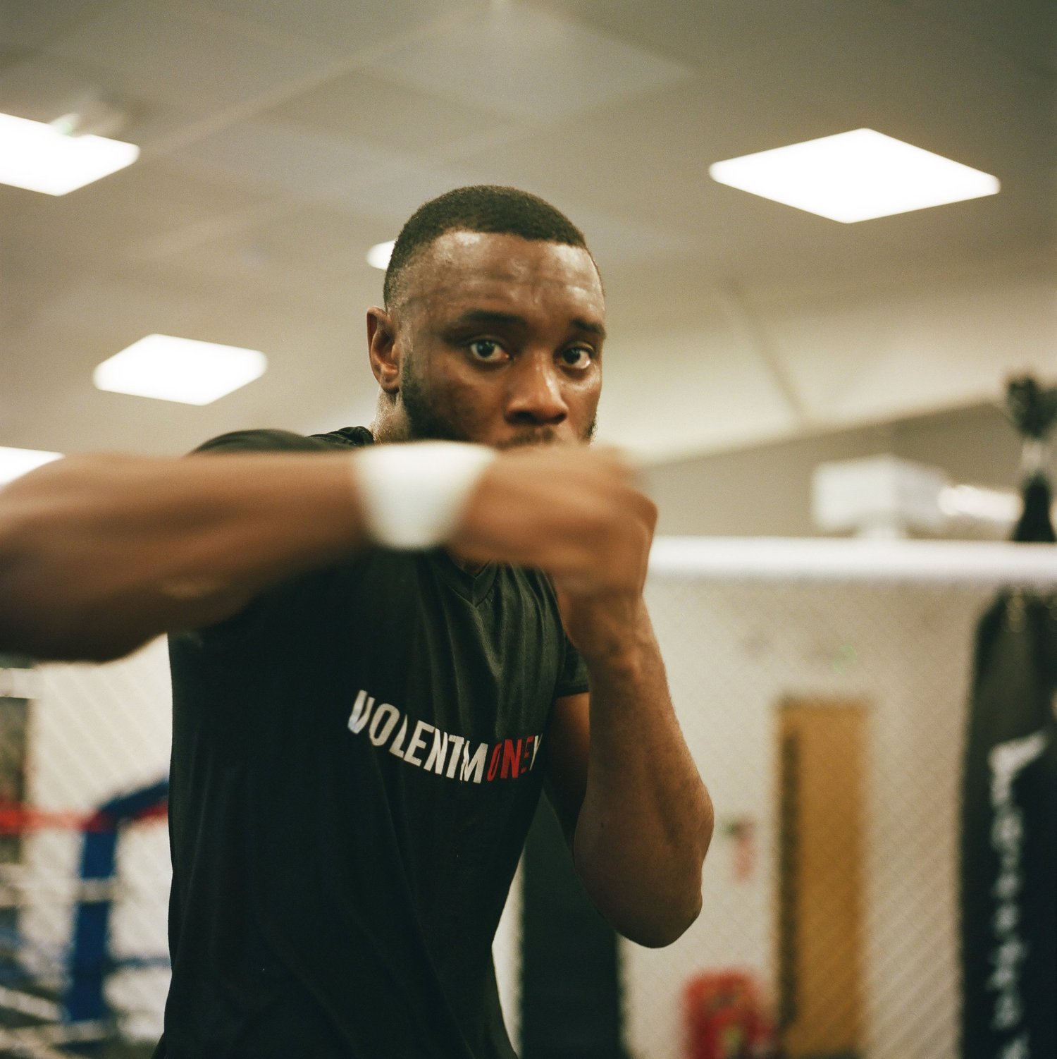 A young man practicing boxing in a gym, wearing a black t-shirt, focusing and throwing a punch.
