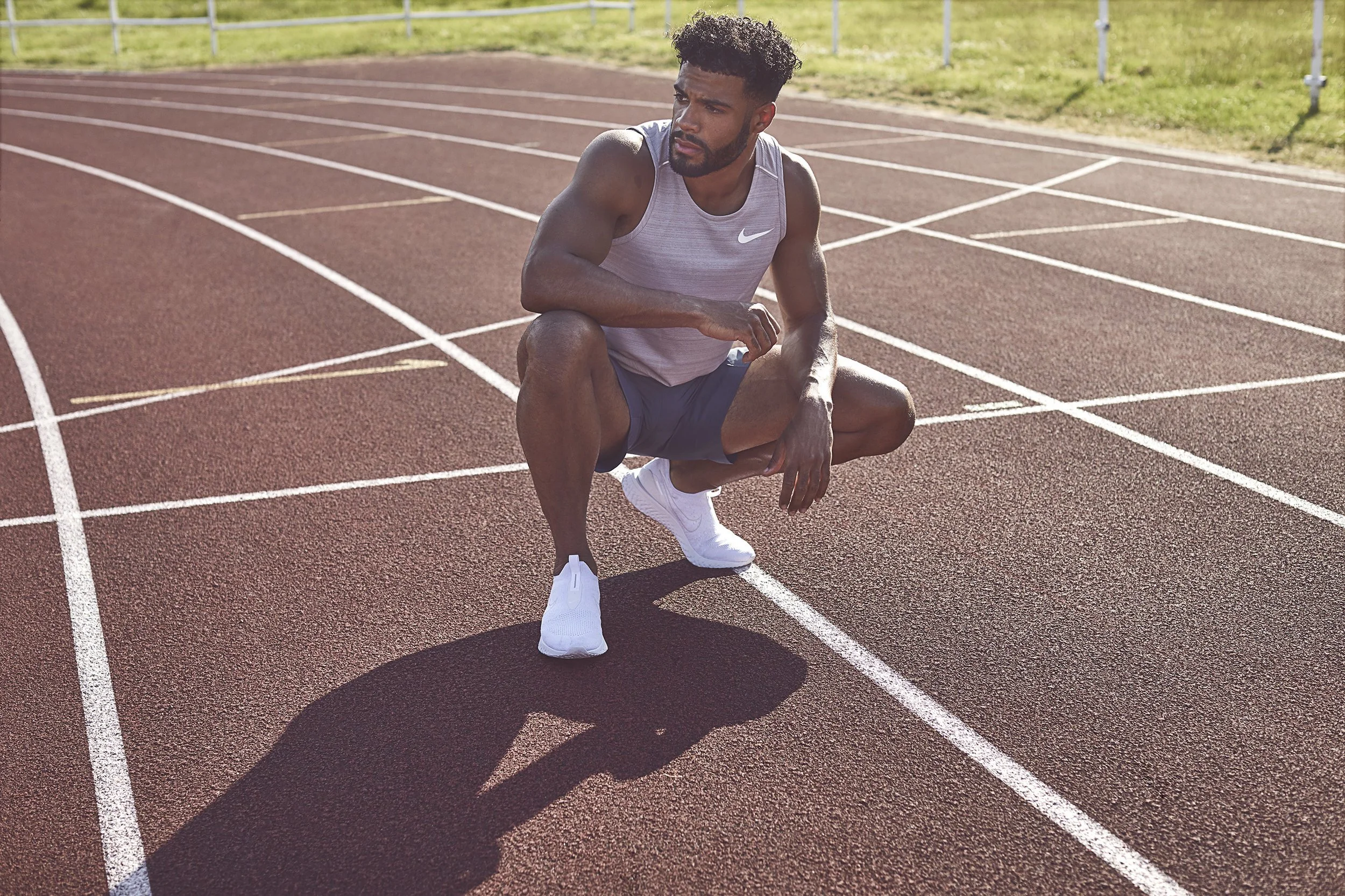 Young male athlete crouching on a running track, wearing athletic gear and white running shoes, preparing for a sprint.