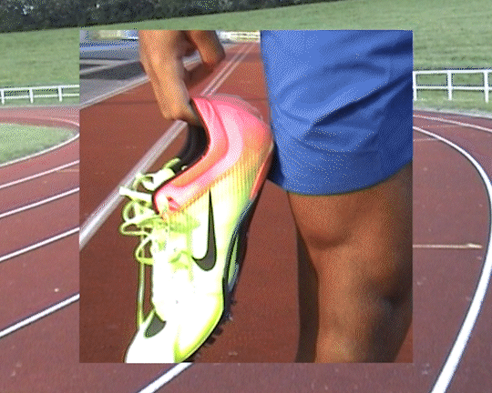 Close-up of a person holding a colorful athletic shoe on a running track, with the person wearing blue shorts.
